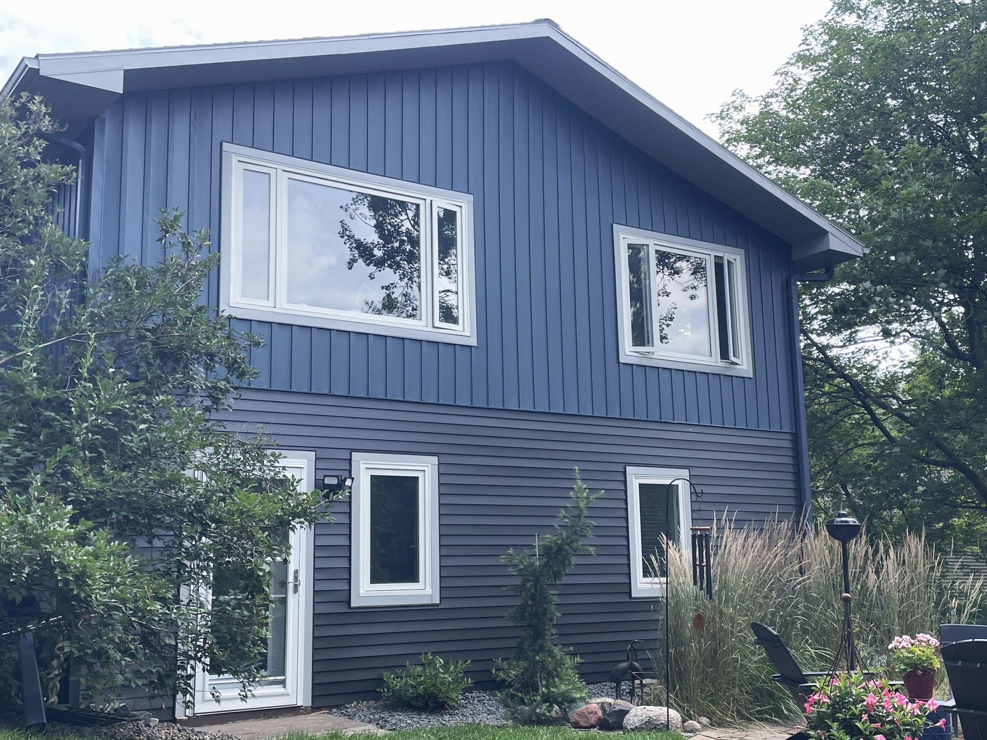 A blue house with white windows is surrounded by trees and bushes.