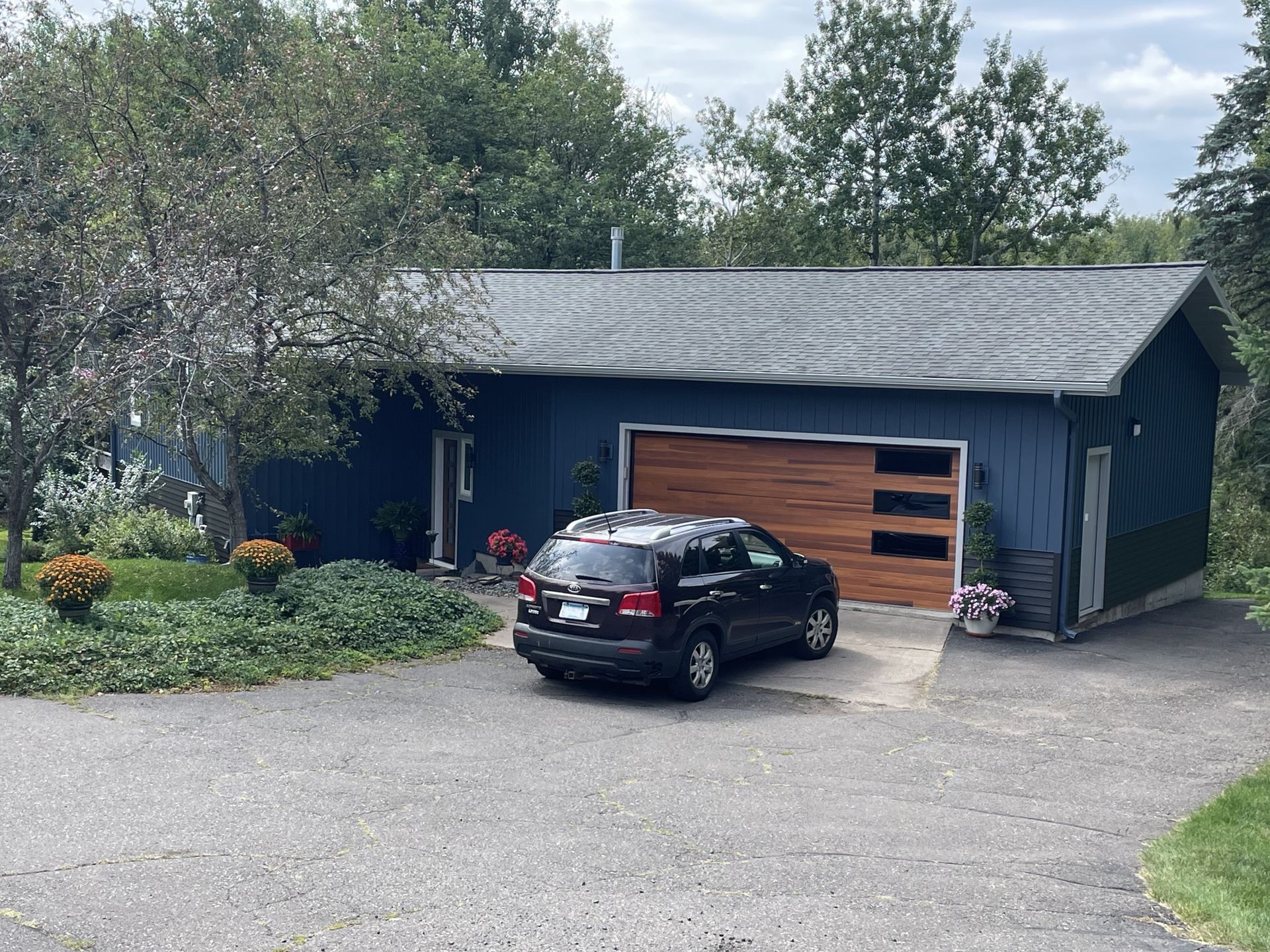 A car is parked in front of a blue house with a wooden garage door.