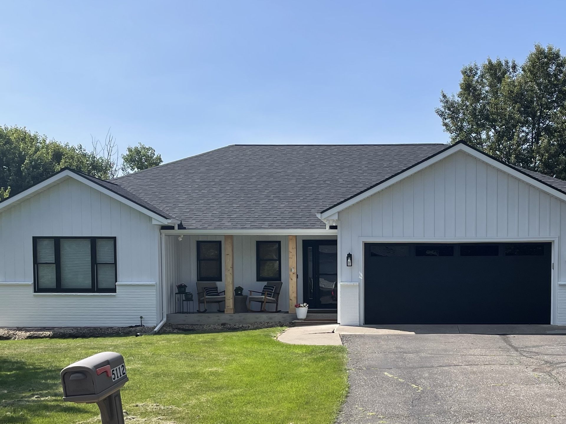 A white house with a black garage door and a mailbox in front of it.
