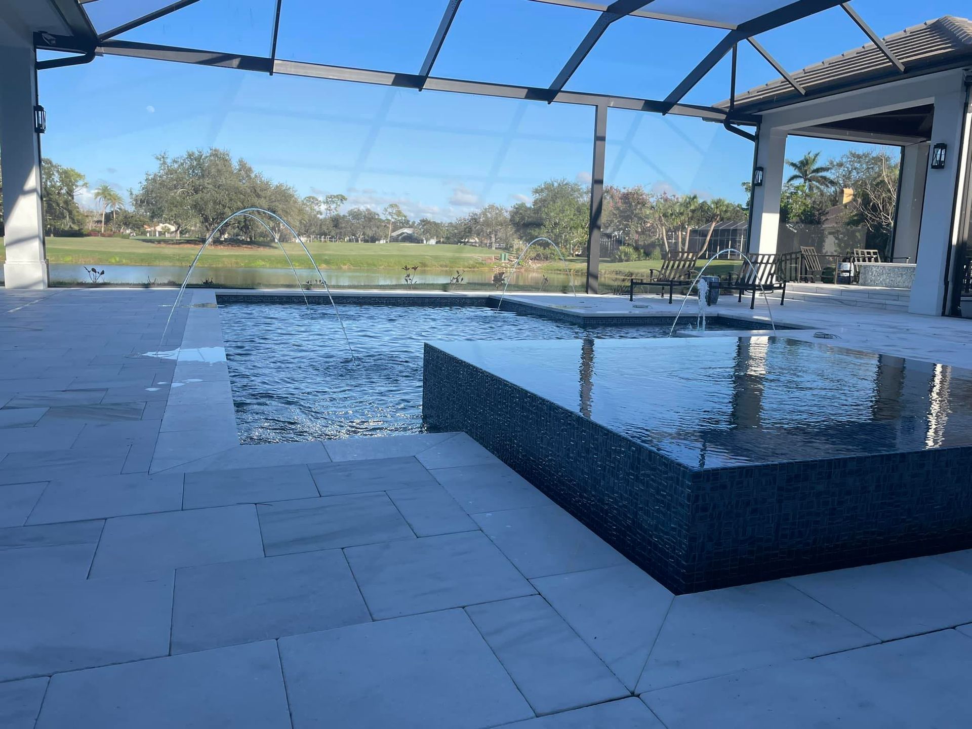 Pool with dark tiled spa, light tiled patio, and view of a golf course, under a screened roof.