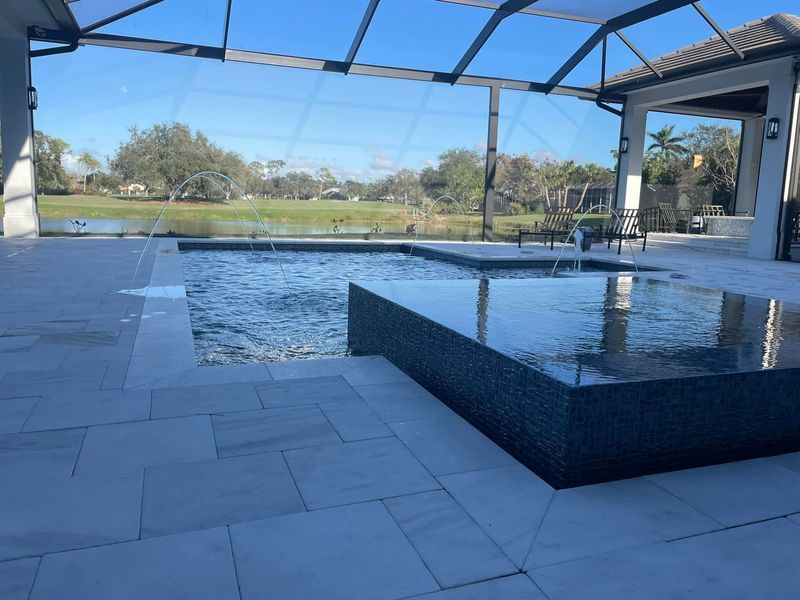 Pool area with tiled deck, fountain, and screened enclosure overlooking a lake.