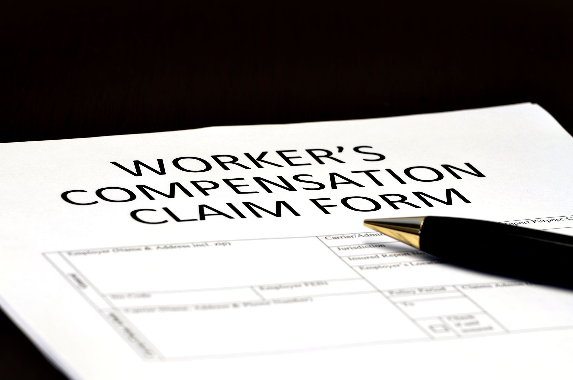 Close-up of a worker's compensation claim form with a black and gold pen resting on top, ready to be filled out.