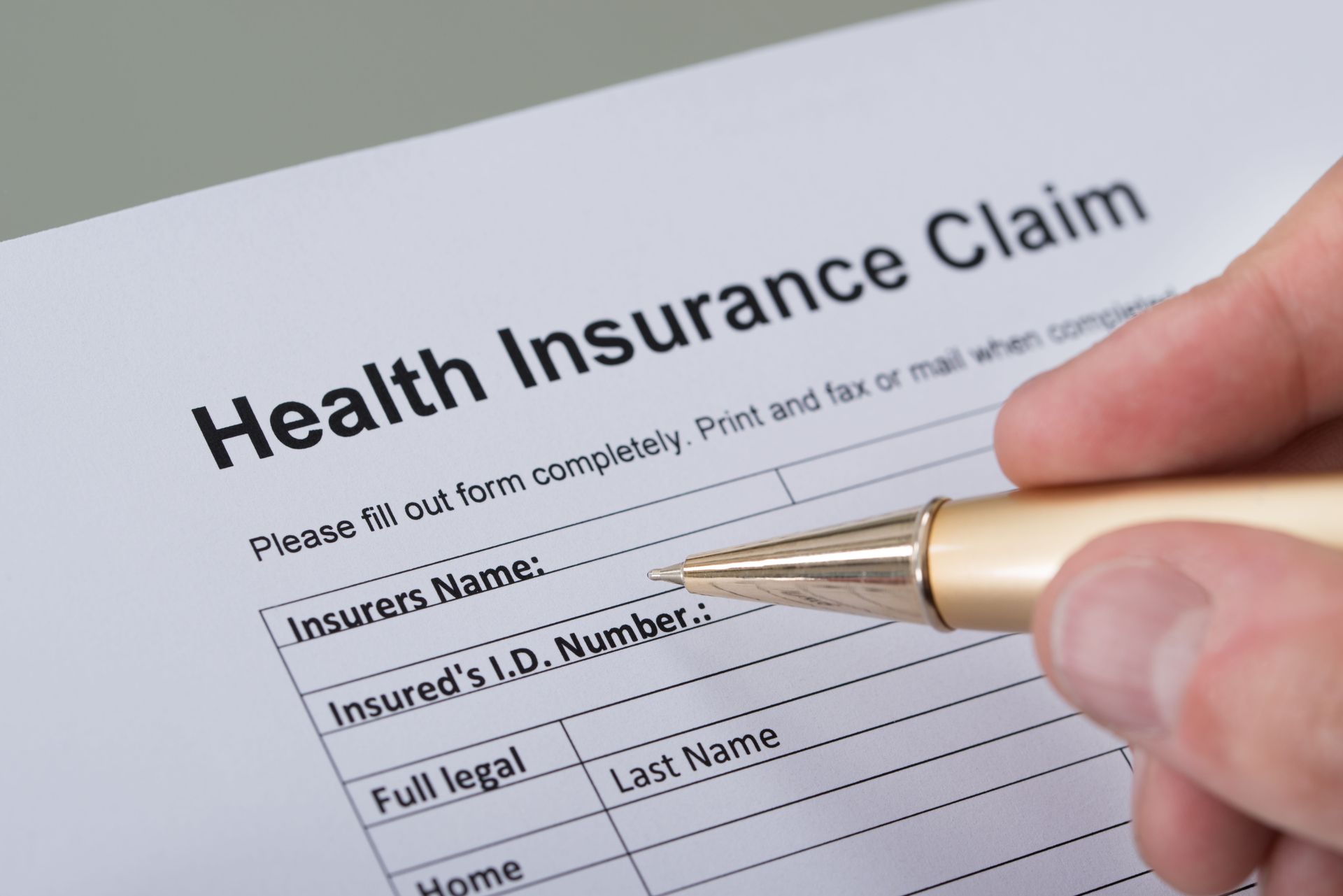 Close-up of a person holding a pen over a health insurance claim form, ready to fill in personal and policy information.