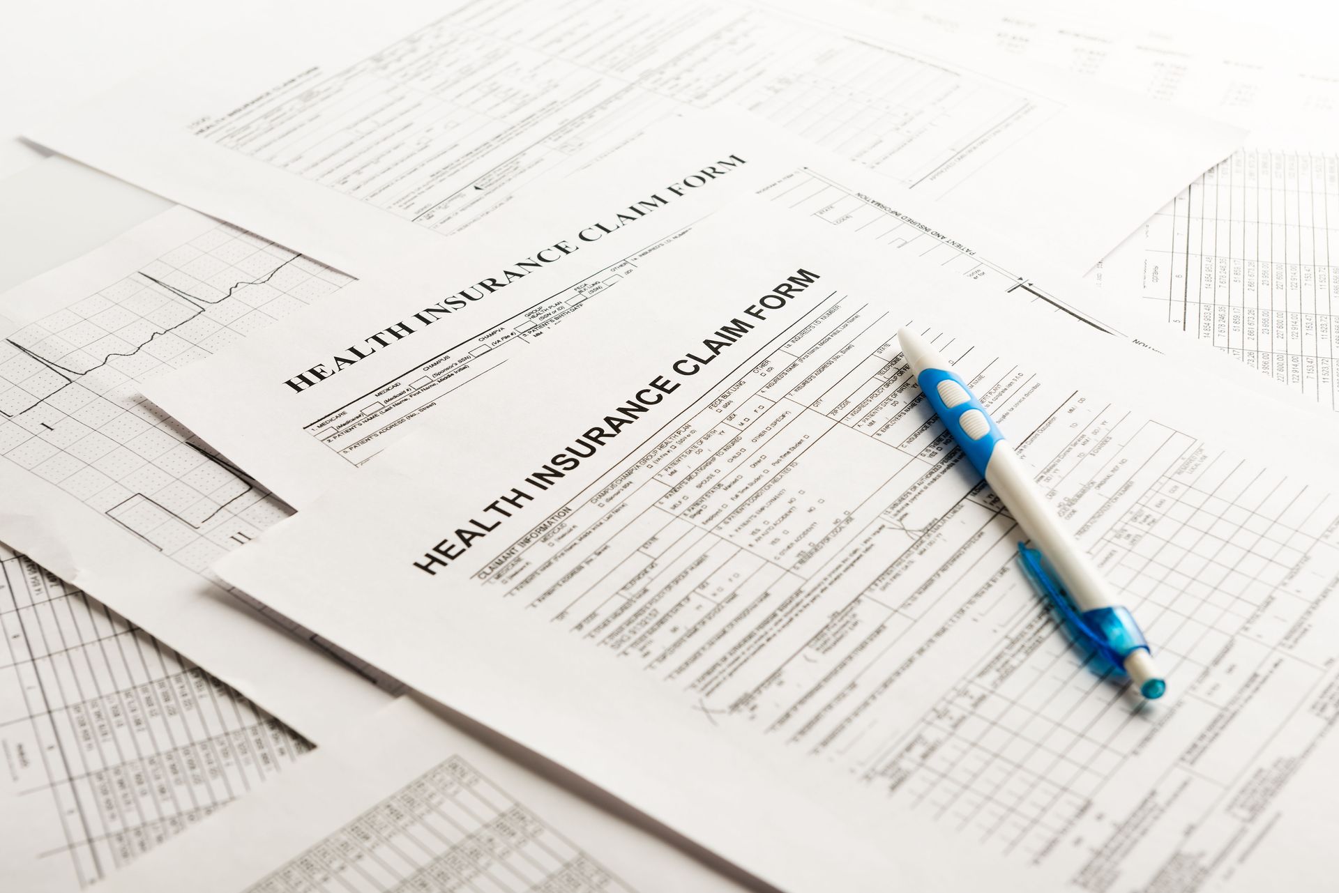 Health insurance claim forms spread out on a table with a blue and white pen placed on top, ready for completion.