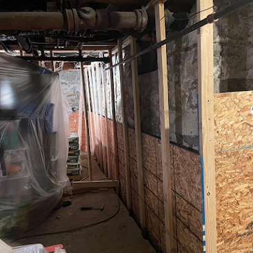 Narrow construction hallway with plastic sheeting, exposed pipes, and wood-paneled walls under renovation