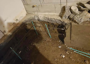 Damaged concrete corner with exposed rebar and debris, showing a broken floor or wall section.