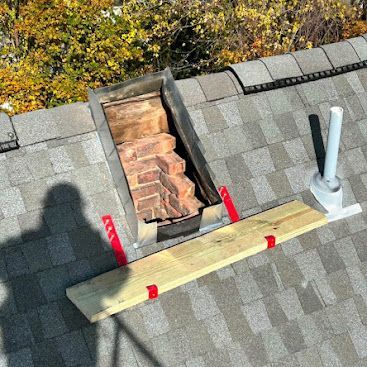 Roof with open chimney repair opening, yellow plank, red brackets, and vent pipes on gray shingles.
