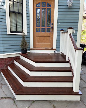 Front steps with dark brown treads and white railings leading to a blue house’s wooden front door