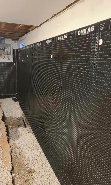 Dark mesh fence lining a narrow outdoor walkway beside a concrete wall and gravel ground.