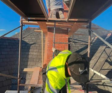 Worker in a neon vest on a roof, installing a chimney flue beside scaffolding.