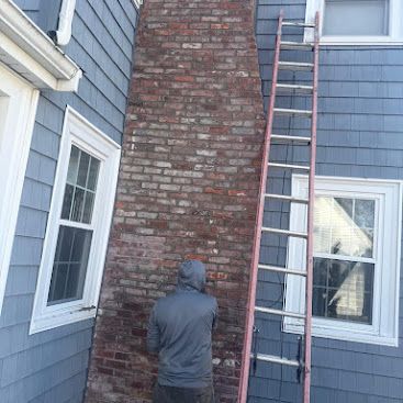 Person working on a brick chimney with a ladder against a blue house exterior.
