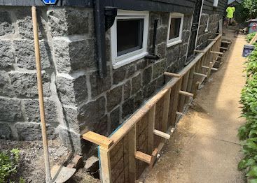 Stone house exterior with wooden ramp under construction along a narrow path