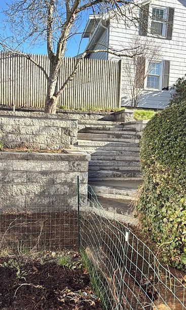 Stone steps leading up to a white house beside a fenced yard and bare tree in a garden.