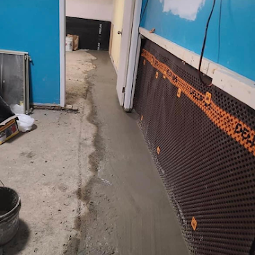 Concrete floor repair in a blue-walled room, with fresh gray cement patching a damaged walkway.
