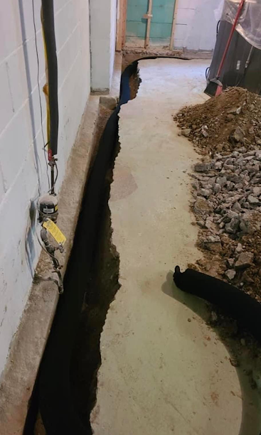 Narrow trench dug along a building wall beside a pile of dirt and debris