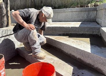 Worker kneeling to smooth concrete on a stepped outdoor patio beside red buckets