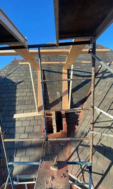 Scaffolding around a brick chimney under construction, with wooden beams against a blue sky.