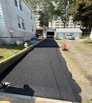 Freshly paved black asphalt driveway beside a house, leading to a detached garage