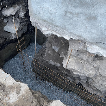 Cracked concrete foundation with exposed rebar and gravel in a damaged excavation area