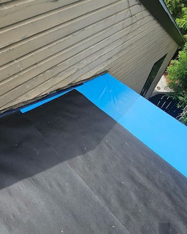 Roof edge covered with black and blue underlayment beside tan siding