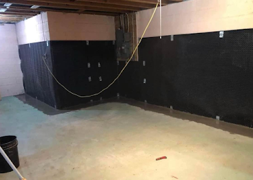 Basement room with black walls, exposed ceiling beams, and unfinished concrete floor.