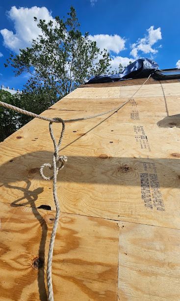Plywood roof under construction with rope, against a blue sky and trees.
