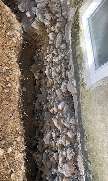Shallow trench filled with rocks beside a house foundation and a window