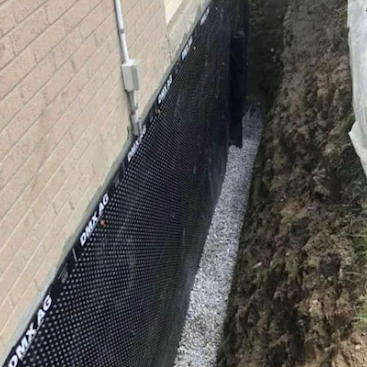 Black mesh fence along a beige brick wall beside a muddy trench