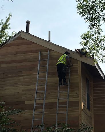 Worker on a ladder repairing the roof of a wooden house exterior