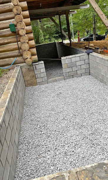 Gravel-filled outdoor patio under a log roof, bordered by low gray cinder block walls