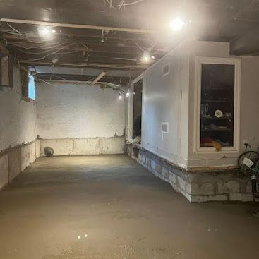 Flooded basement interior with muddy water, exposed ceiling beams, and a white utility room on the right