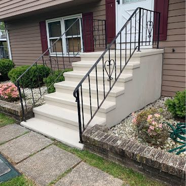 Front steps with white railings leading to a townhouse entrance, beside a paved walkway and flower beds