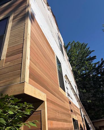 Modern wooden house exterior with slanted roof and a ladder beside it under a blue sky