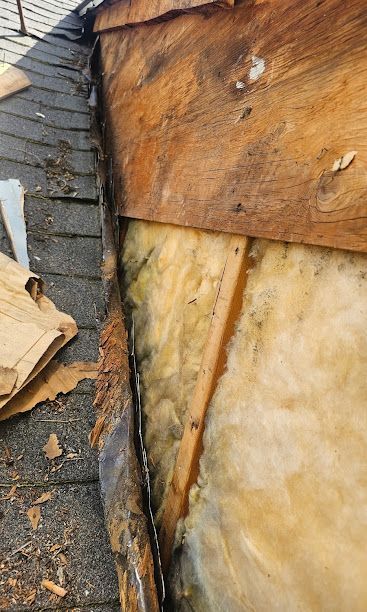 Close-up of damaged roof and wall with exposed wood, insulation, and torn shingles