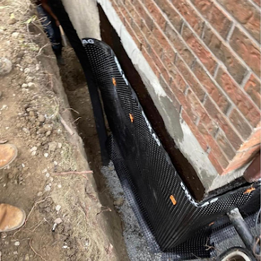 Black drainage pipe along a brick foundation trench with dirt and gravel