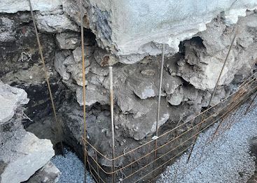 Collapsed concrete edge with exposed rebar and gravel near a damaged excavation site