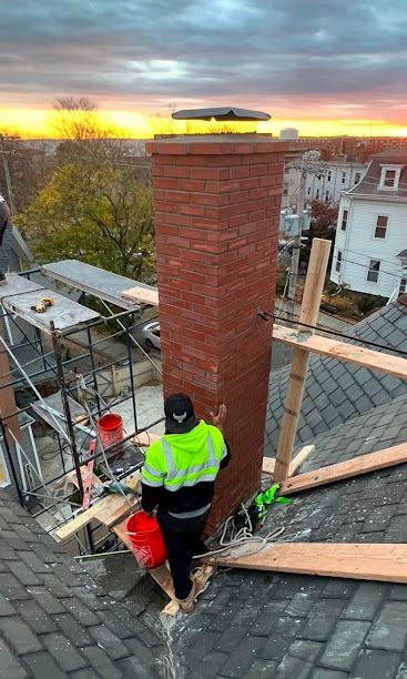Worker in neon jacket on a roof beside a brick chimney at sunset