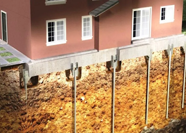 House foundation with steel support posts beside a dug-out slope and exposed soil