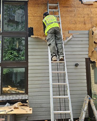 Worker on a ladder repairing exterior siding on a house.