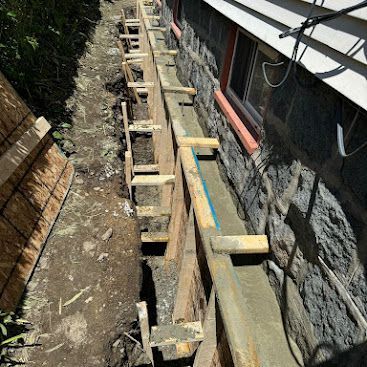 Wooden formwork and concrete beam along a house wall in a narrow outdoor construction area