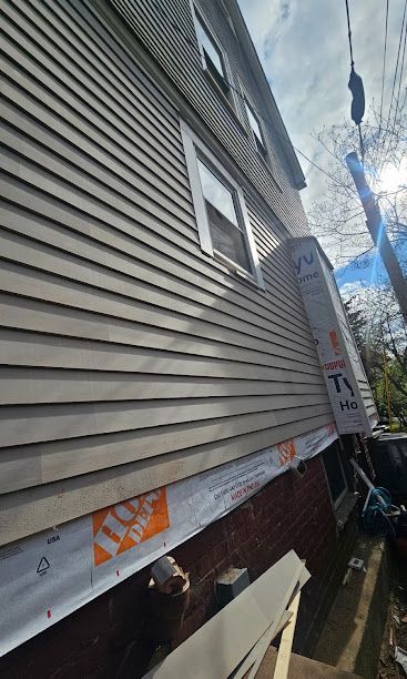 Side view of a house with beige siding, a basement window, and a narrow alley along the foundation