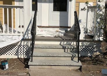 Front porch steps with black metal railings leading to a white front door and entrance.