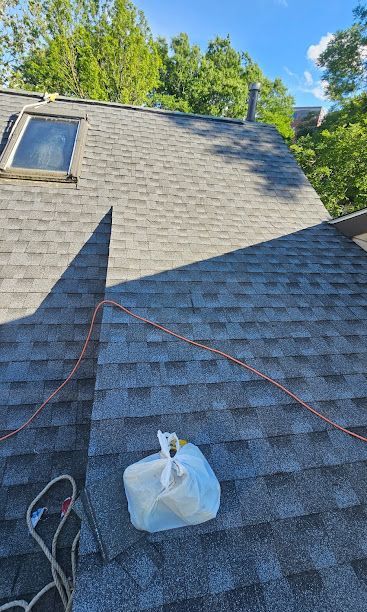 Roof with gray shingles, skylight, and a bag on the surface, with a rope or line across the slope.