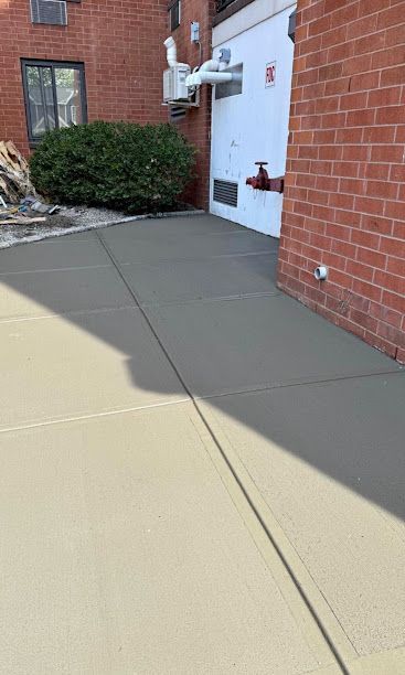 Concrete sidewalk beside a brick building with a white door and bushes nearby