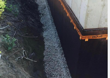 Close-up of a building foundation with black drainage mesh beside a gravel trench and soil.