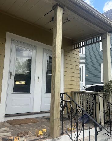 Front porch with white door, wooden post, and black iron railing on a small house.