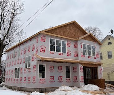 Two-story house under construction wrapped in house sheathing, with snow on the ground.