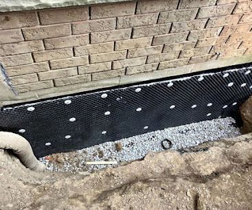Black waterproofing membrane and gravel drainage strip along a brick foundation wall.