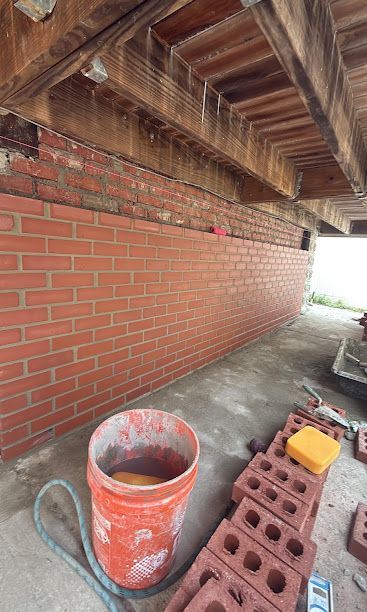 Brick wall under exposed wooden roof with construction bucket and stacked cinder blocks on a concrete floor