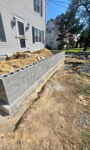 Concrete block retaining wall beside a house, with dirt and construction debris along the side yard.